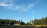 Op de achtergrond het huis en de schuren. De 4 verticals voor de 80meterband op de voorgrond, elk 20m hoog. In het midden de 60m hoge en draaibare mast vol enorme richtantennes.